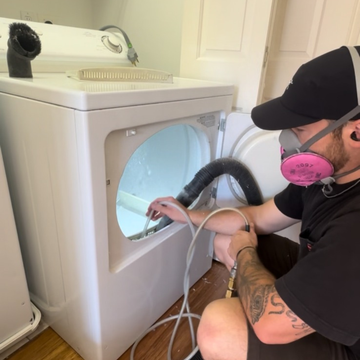 Technician cleaning the interior of a dryer, removing lint from around the heating element and blower, emphasizing dryer maintenance and fire prevention.
