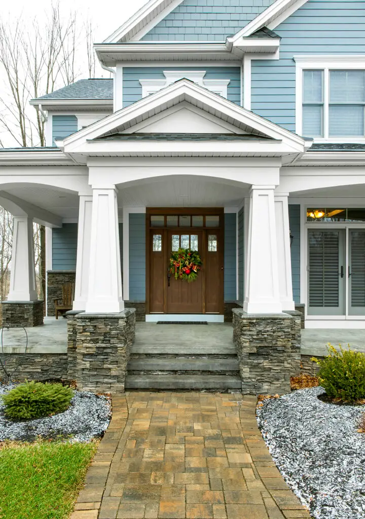 Christmas wreath on front door of a blue house with stone pillars and landscaped pathway, symbolizing home safety and welcoming atmosphere.