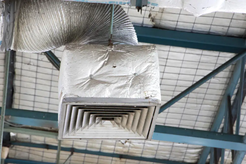 Air duct vent with metallic cover and flexible ducting in a residential or commercial setting, relevant to air duct and dryer vent cleaning services in Newburyport, MA.
