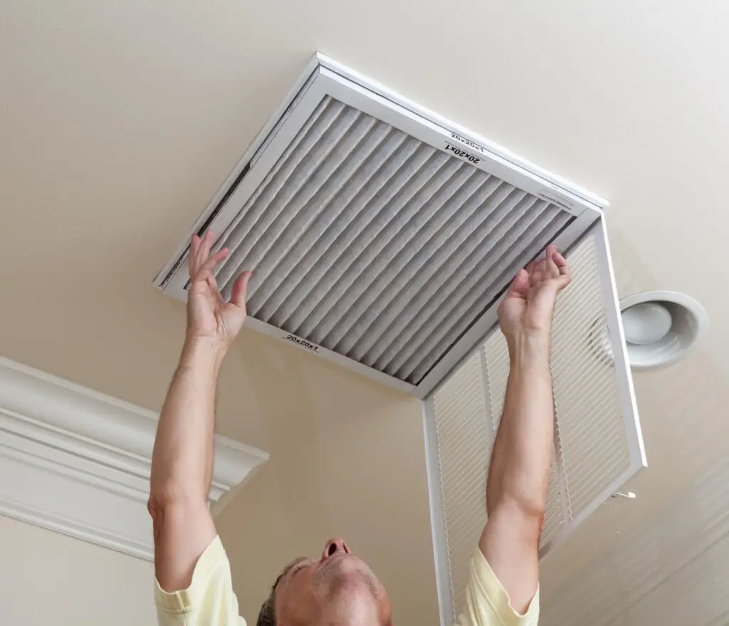 Person reaching up to remove an air filter from a ceiling vent, emphasizing home maintenance and air quality improvement.