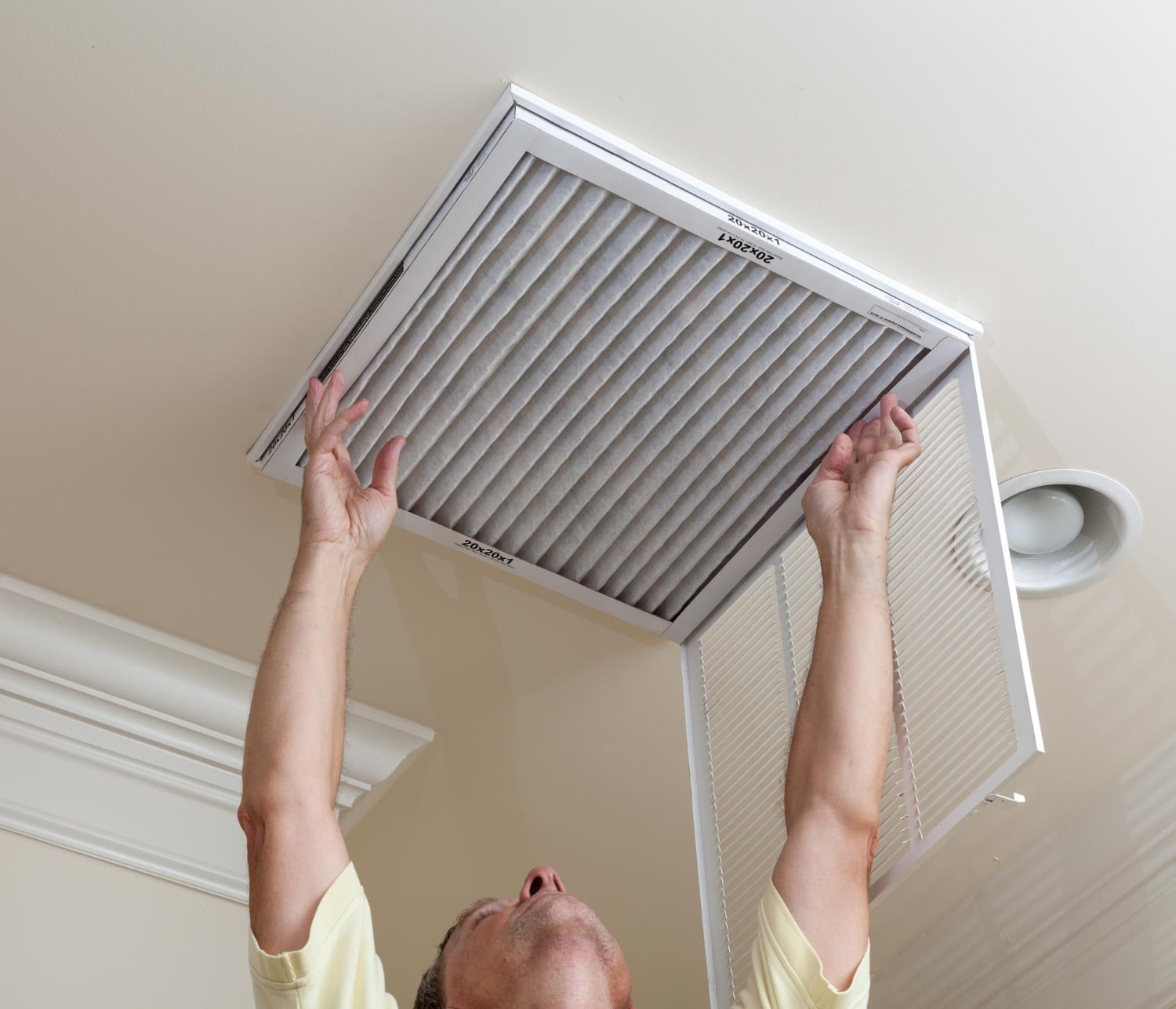 Person reaching up to replace an air filter in a ceiling vent, emphasizing air quality and HVAC maintenance for healthier indoor air.