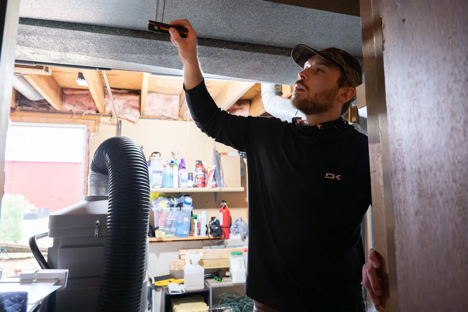 Technician inspecting HVAC ductwork with flashlight, demonstrating professional air duct cleaning process in a residential setting.