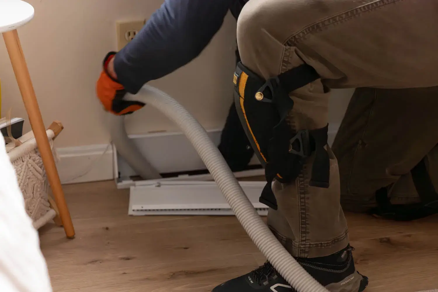 Professional technician cleaning air ducts with vacuum hose in New England home environment.