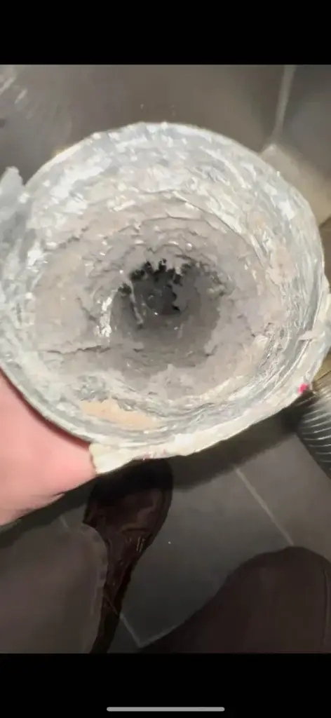 Close-up of a hand holding a lint-filled dryer vent duct, highlighting excessive lint buildup, an indicator of potential fire risk and the need for professional cleaning services.