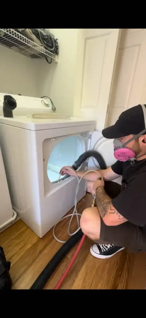 A technician cleaning the interior of a washing machine using a vacuum hose.